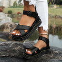 Black criss-cross platform sandals with adjustable buckle ankle strap and chunky flatform sole, angled view.