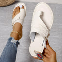 White cream leather flat sandal with buckle cross-strap and toe-ring loop, overhead angled view on grey background.
