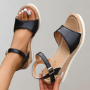 Black espadrille wedge sandals with buckle ankle strap, natural tan jute-wrapped wedge midsole and white rubber outsole, angled front view.
