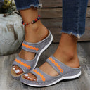 Grey mesh platform slide sandals with orange embroidered wave trim and white sole, worn with distressed jeans, angled view.