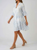 White mini dress with blue paisley print, V-neck, and tiered skirt, angled view.