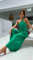 Green asymmetrical strapless jumpsuit with high waistline, angled view on a white patio.