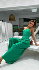 Green asymmetrical strapless jumpsuit with high waistline, angled view on a patio.