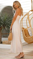 Beige asymmetrical strapless jumpsuit with high waistline, angled view on outdoor patio.