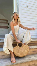 Beige asymmetrical strapless jumpsuit with high waistline, angled view on wooden steps.