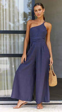 Navy asymmetrical strapless jumpsuit with wide legs, front view on a windowed background.