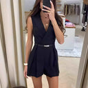 Black sleeveless overall with V-neck, belted waist, and pleated shorts, front view in a store.