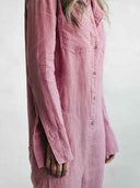Pink long-sleeve jumpsuit with chest pocket and button closure, angled side view.