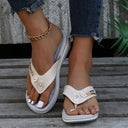 Beige perforated thong sandal with metallic stud detail and low wedge flatform sole, angled front view worn on feet.