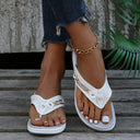 White cushioned wedge thong sandal with perforated strap and stud detail, low flatform sole, angled view on feet.