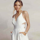 White backless V-neck spaghetti strap jumpsuit with cut-outs, model with hands in pockets, front view.