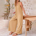 Tan baggy V-neck jumpsuit with side pockets, shown on a model holding a mug, angled view.