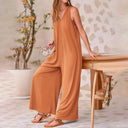 Rust orange baggy V-neck jumpsuit with side pockets, front view on a patterned background.