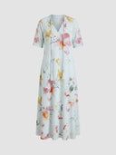 Beatrice Floral V-Neck Maxi Summer Dress in Sky Blue with watercolour floral print, short sleeves and tassel tie V-neckline, A-line silhouette, front view on grey background.