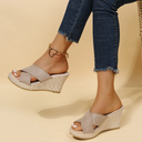Beige cross-strap wedge mule sandals with woven espadrille platform sole, styled with dark jeans on neutral background.