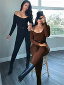 Two women wearing off-shoulder ribbed unitard jumpsuits, one standing in black and one seated in brown, full-body view.