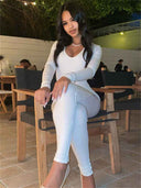 Woman in white seamless ribbed unitard jumpsuit, seated at night, angled view.