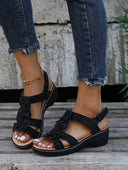 Black floral appliqué low wedge sandals with chunky block sole and slingback ankle strap, angled front view.