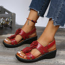 Red low wedge sandals with 3D floral appliqué straps and black chunky sole, angled front view.