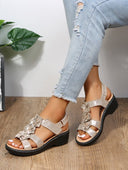 Beige floral appliqué low wedge sandals with ruffled strap detail and contrast white midsole, angled view.