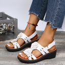 White low wedge sandals with floral cutout strap detail and black chunky platform sole, front view.