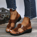 Brown low wedge sandals with 3D flower appliqué straps, ankle buckle, and black chunky platform sole, angled view.