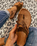 Brown toe-ring buckle flat sandal with cushioned footbed, held in hand over leopard-print fabric background — angled overhead view.