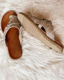 Pair of brown toe-ring buckle flat sandals with cushioned soles, angled overhead view on textured surface.