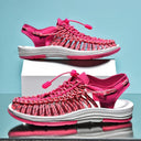 Bright pink woven sandals with white midsole and cord closure, shown in front and side views on white box against blue background.