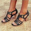 Black strappy high heel sandals with gold buckle details and cork heel, front angled view on woven background.