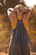 Woman in black jumpsuit with mustard ribbed top, back view, outdoor setting.