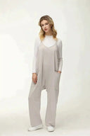 Woman in light gray jumpsuit with large pockets over white long-sleeve top, front view.