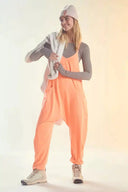 Model wearing peach Cela jumpsuit with gray long-sleeve shirt and beanie, front view.