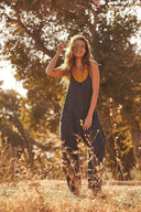 Woman in a charcoal jumpsuit with a yellow top underneath, standing outdoors in tall grass, front view.