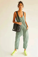 Green scoop-neck jumpsuit with drop crotch and pockets, worn by a model with a black bag, front view.