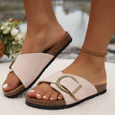 Blush pink flat slip-on sandals with wide adjustable antique-gold buckle strap and cork flatbed sole, angled front view on model outdoors.
