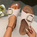 Cream flat slip-on sandals with adjustable buckle strap and cushioned cork-look footbed, angled top-down view.
