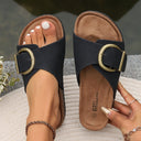 Black flat slip-on sandals with adjustable antique-gold buckle strap and tan cork-look footbed, angled top-down view.