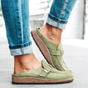 Green closed-toe flatform mules with buckle strap and cork sole, worn with rolled-cuff jeans, angled side view.