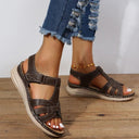 Brown low wedge sandals with cushioned cream sole and contrast stitching, worn on feet with distressed denim jeans, angled front view.
