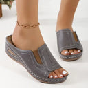 Grey open toe wedge mule sandals with white contrast stitching, shown on foot against white background.