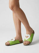Light green flatform slide sandals with white heart cutout on strap, worn on feet, angled view.
