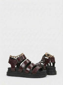 Pair of wine red chunky platform sandals showing gladiator strap construction, gold chain hardware and black rubber outsole, angled view on white.