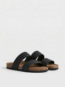 Black flat double-strap slide sandals with cork-look footbed, angled view on white background.