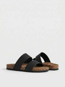 Black two-strap slip-on flat sandals with cork footbed and dark rubber sole, three-quarter view on white background.