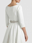 Daisy white A-line midi dress showing high-low hem, centre-back zip closure and rhinestone jewelled belt detail, angled rear view.