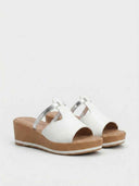 Pair of white wedge mule sandals with silver cross-strap and tan platform wedge sole, angled product view on white background.
