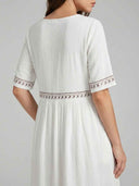 White embroidered maxi dress showing gathered empire waist and short sleeves, angled back view.