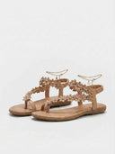 Beige flat sandal with daisy flower appliqué straps and gold-tone ankle chain, angled three-quarter view on white background.