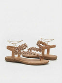 Pair of beige floral flat thong sandals with daisy appliqué and gold chain anklets, angled top-side view on white background.